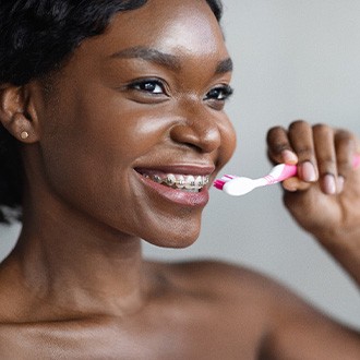 Woman with braces smiling while brushing teeth