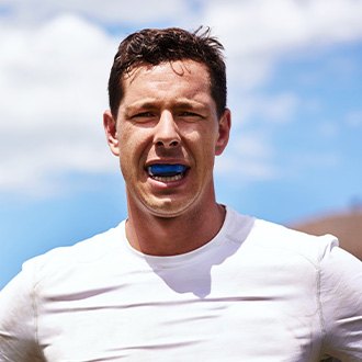 Man with blue mouthguard smiling outside